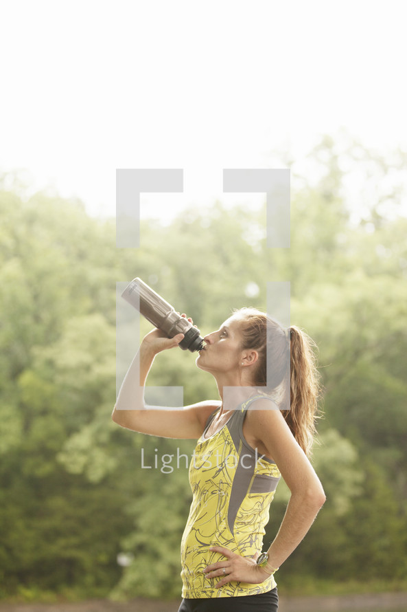 Woman drinking from a sports bottle after a morning run. 