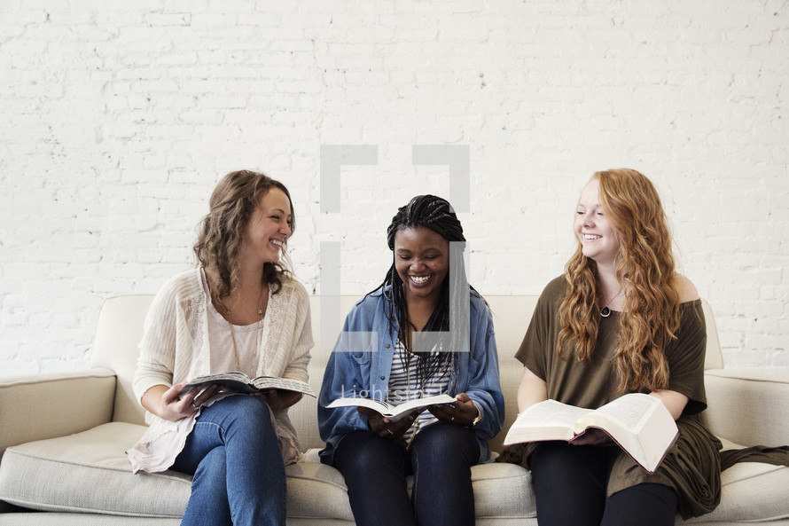 young women sitting on a couch talking, laughing, and reading bibles 