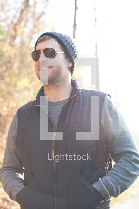 smiling man standing outdoors in sunglasses and a wool cap 