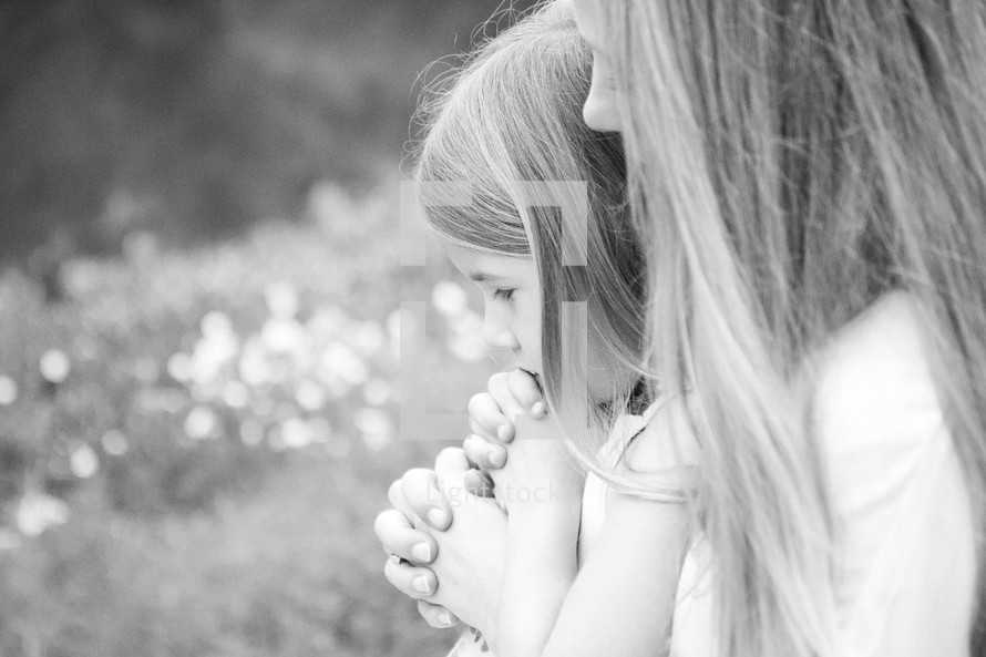 Mother and daughter in prayer outdoors.