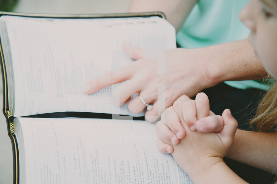 Mother and daughter in prayer while reading the Bible.