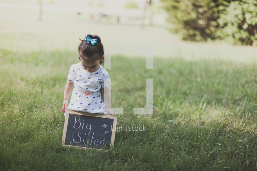 Girl standing outside in the grass holding a "big sister" chalkboard sign.