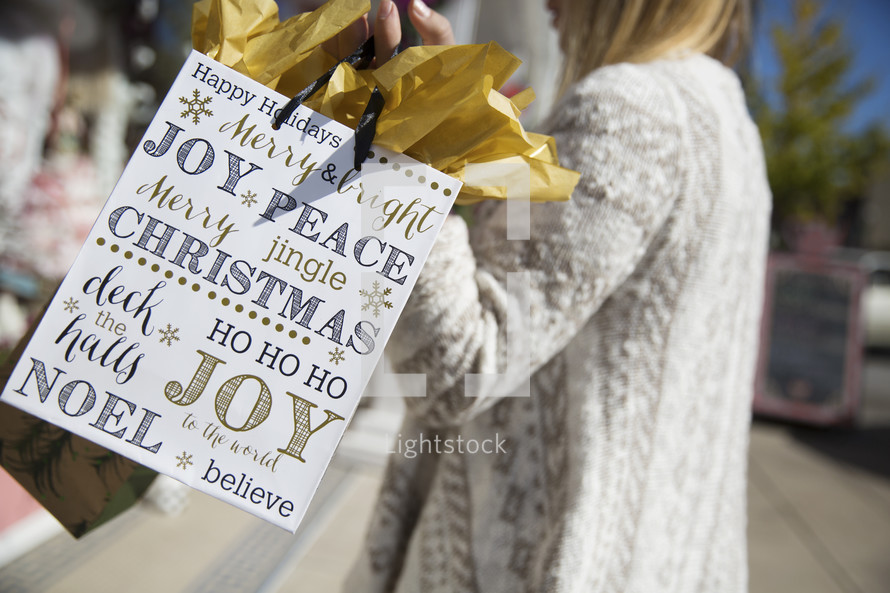 woman carrying Christmas gift bags through town.