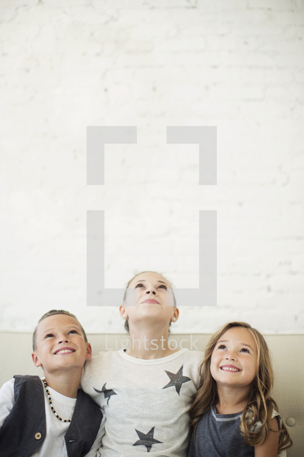 kids sitting together on a couch looking up.