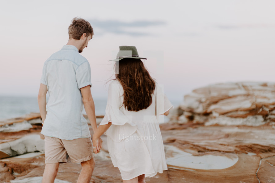 a couple walking on a rocky beach holding hands 