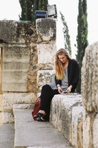 A woman sitting on a stone wall reading a Bible in Jerusalem