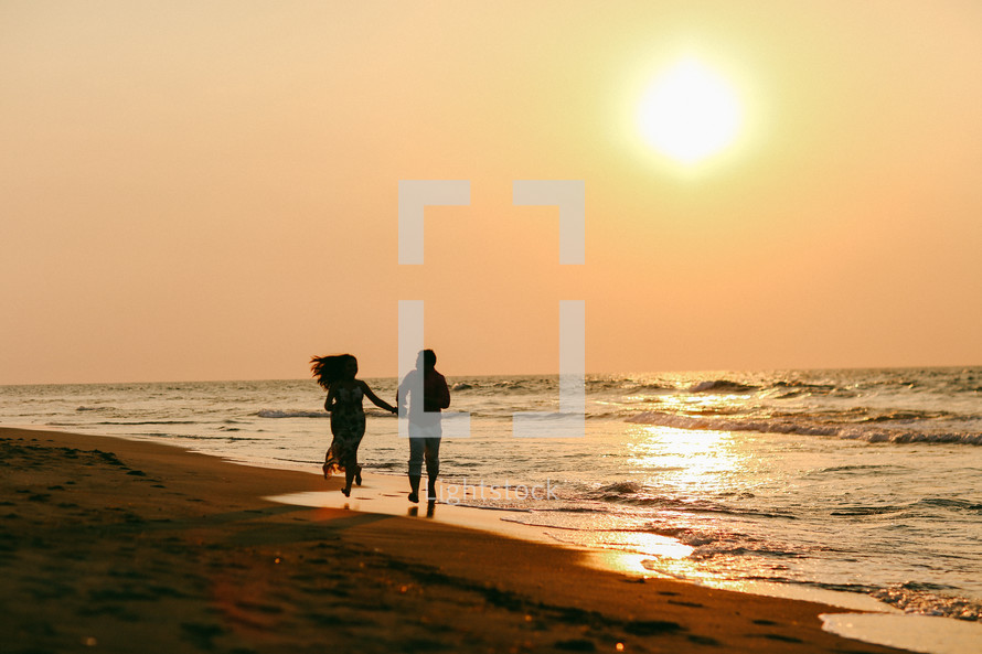 a couple running holding hands on a beach at sunset 