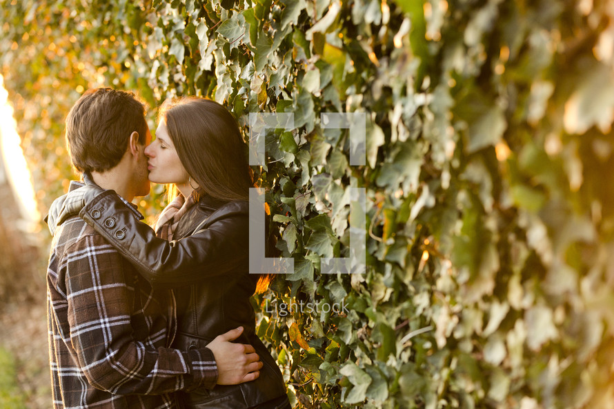 woman kissing a man on the cheek in front of an ivy covered wall