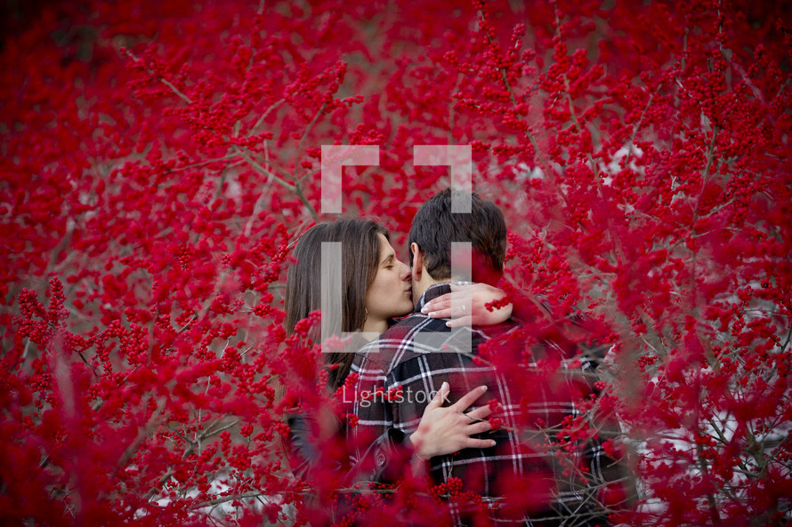 a couple kissing between branches covered with red berries