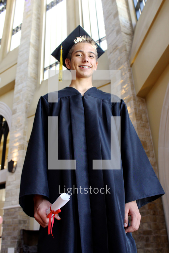 teen boy in his cap and gown holding his diploma 