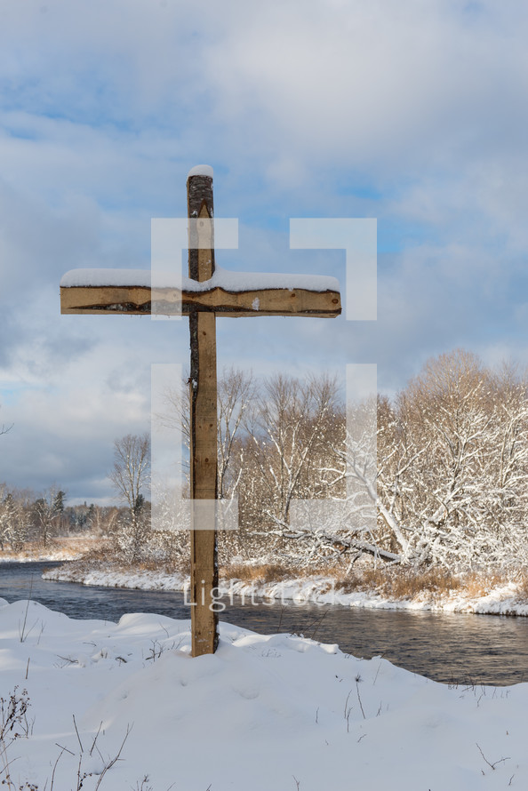 cross with snow on a riverbank 