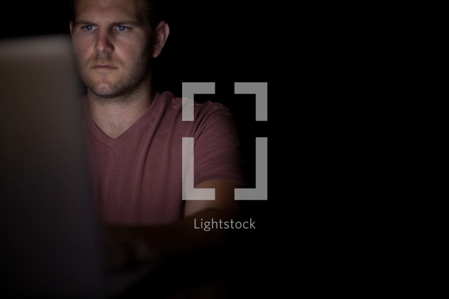 A man illuminated by the light from a computer.