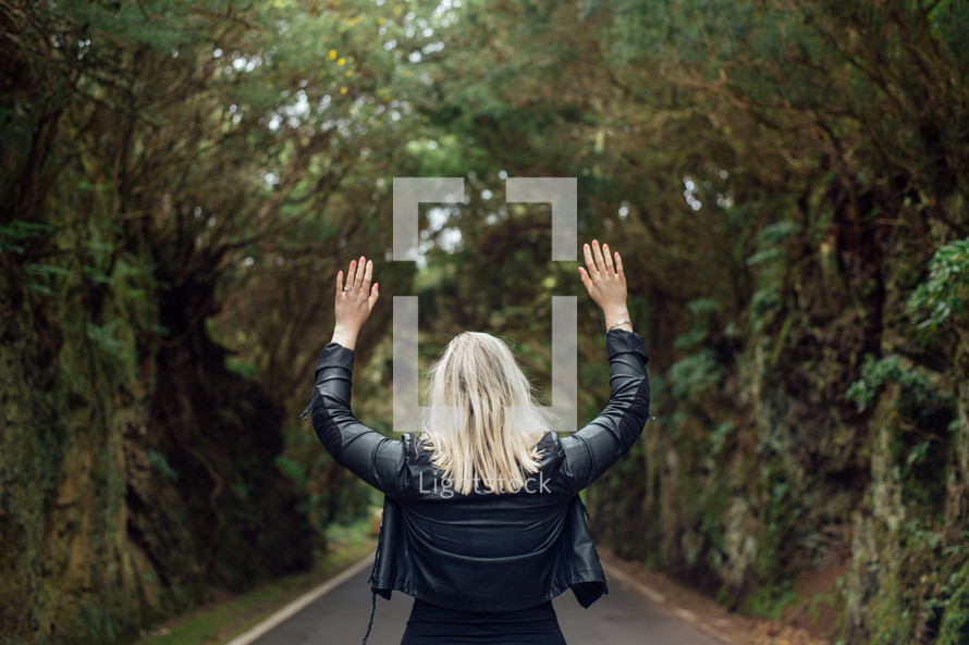 Woman standing on the road in the forest with raised hands.