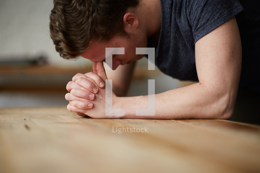 a man with his head on praying hands on a table 