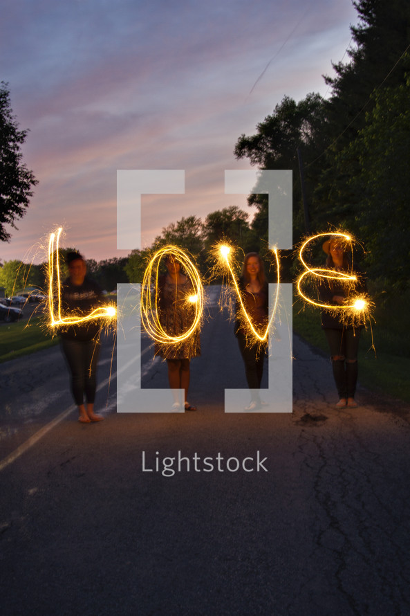 Four women spelling "love" with sparklers.