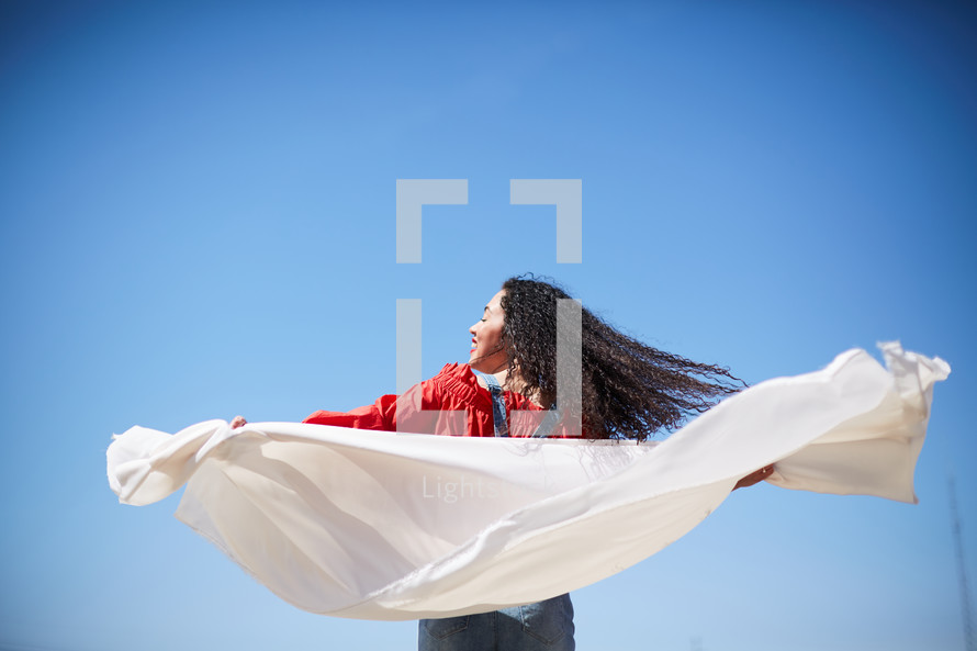 a woman with outstretched arms holding a white sheet 