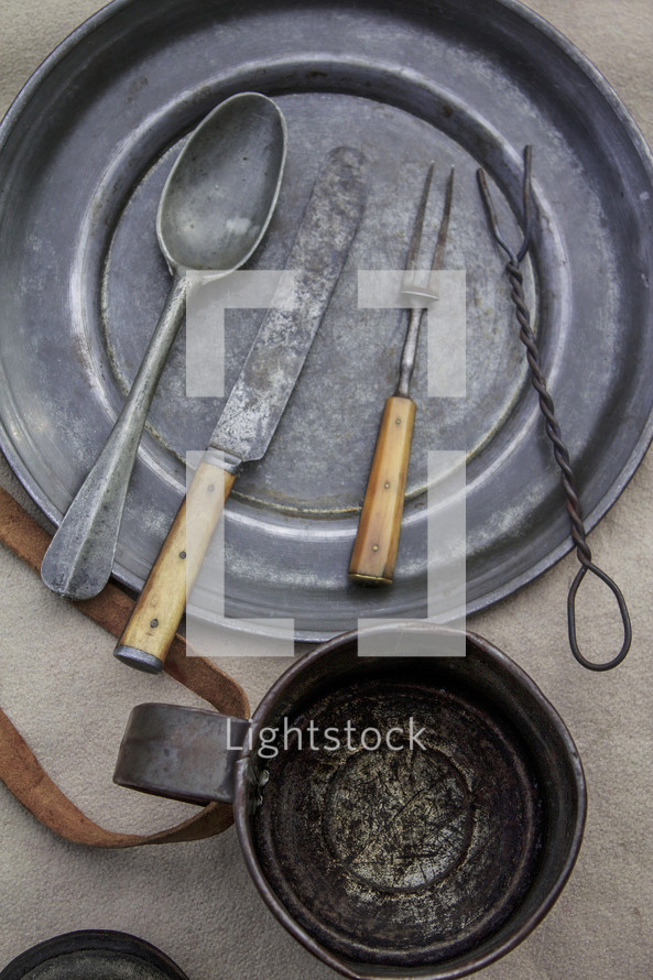Primitive place setting" metal utensils, plate and cup.