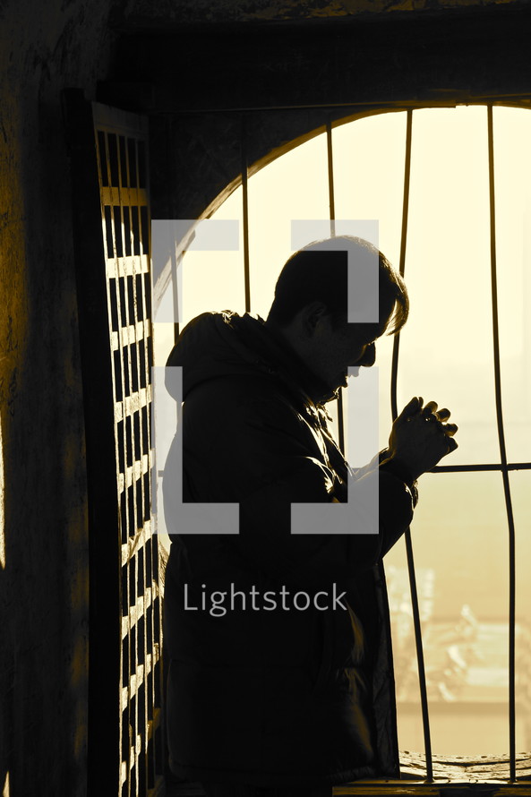 Silhouette of a Chinese church leader in prayer in front of a barred window