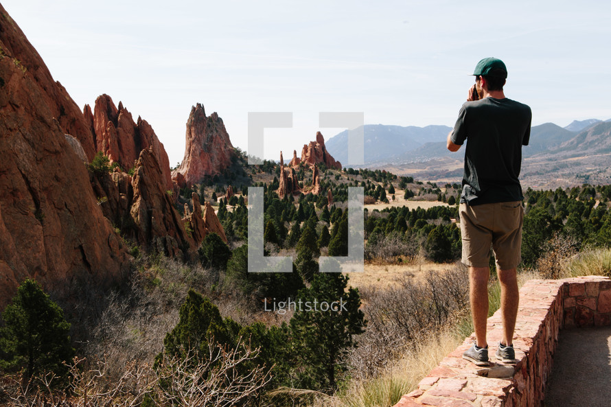 man standing on a ledge looking out at red rock formations