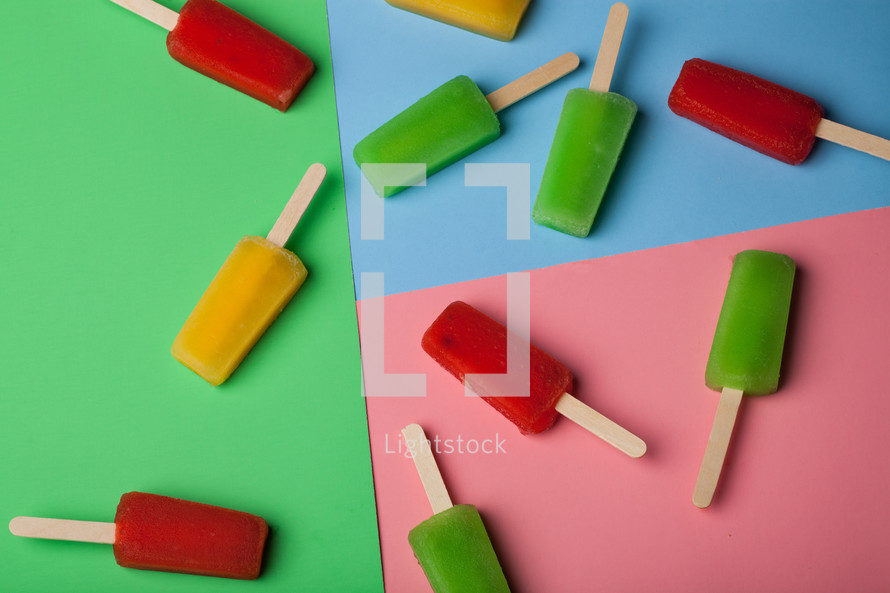 Brightly colored popsicles arranged on different colored paper.