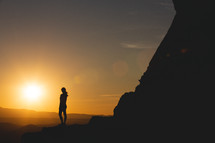 silhouette of a woman standing at the edge of a mountain at sunset 