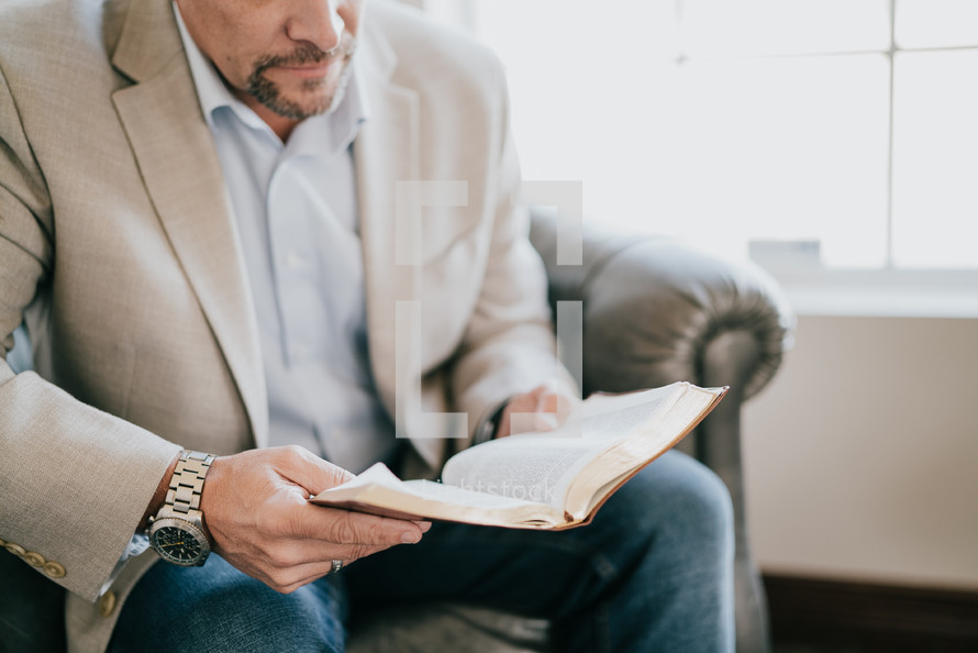 man in a suit sitting reading a Bible 