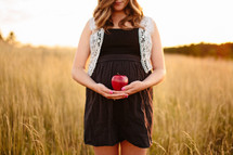 woman standing in a field cradling an apple