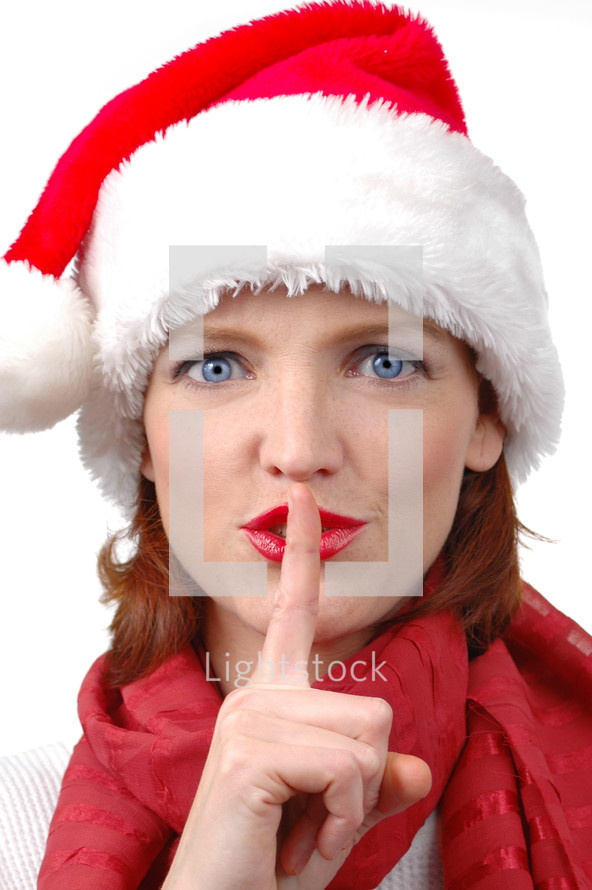 A woman in a Santa hat with her finger to her lips saying "sshhh."