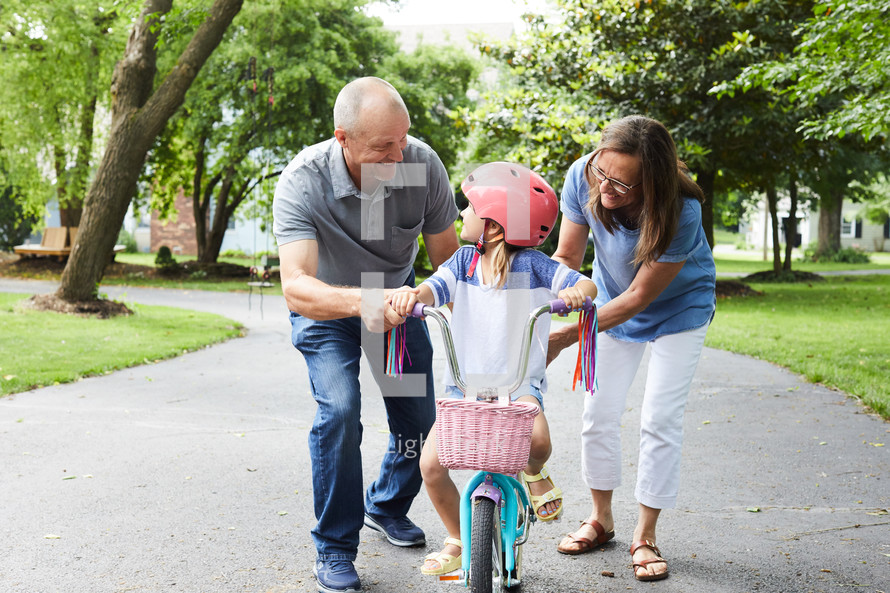 grandparents helping a young girl learn to ride a bike 