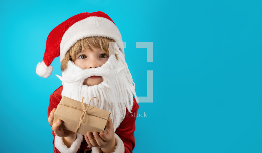 Excited boy in Santa costume with beard holding gift box with bow. Child, Happy kid with present. Blue Christmas background. Copy space, banner. High quality photo