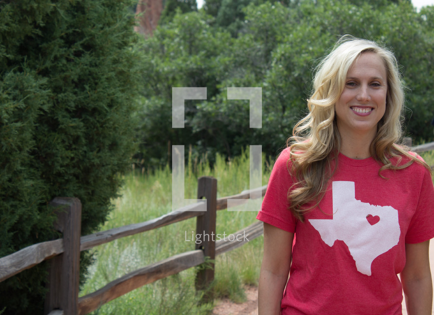 woman with a Texas t-shirt standing by a fence 