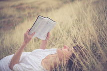 Woman laying in a field of grass reading the Bible.