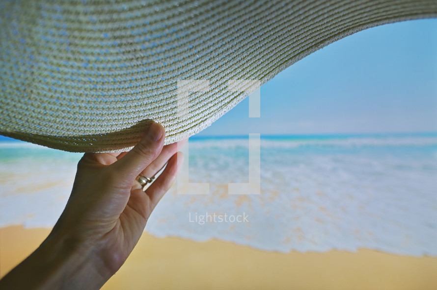 Wide angle of Woman Relaxing On Beach Holding Sun Hat and Sea in Background