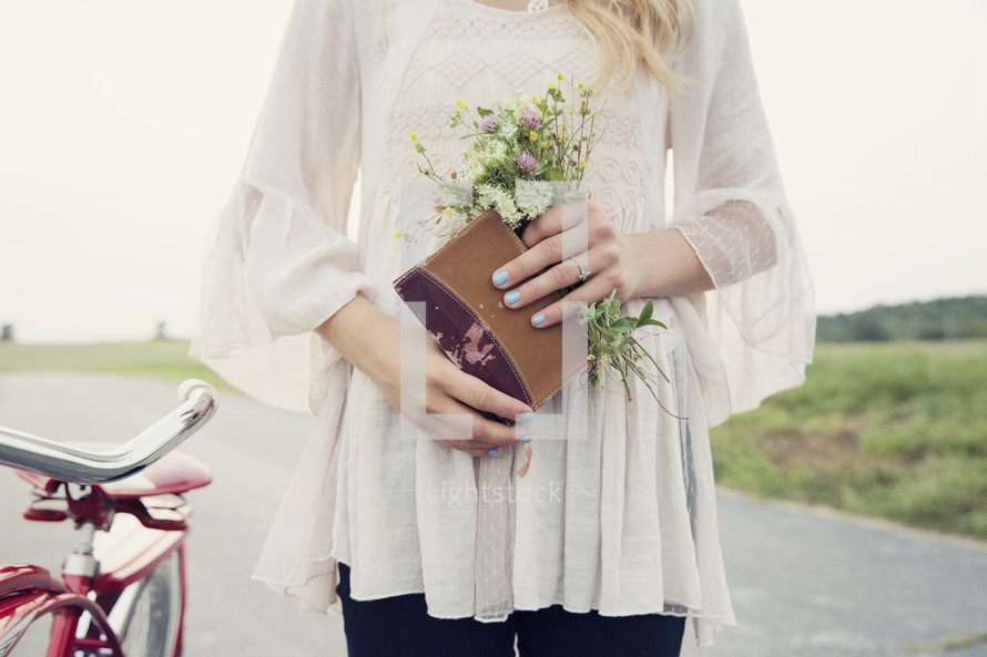 woman holding a journal and flowers standing next to a bike 