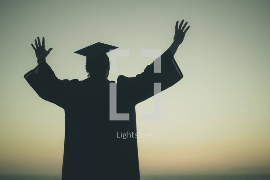 silhouette of a graduate with his hands raised 