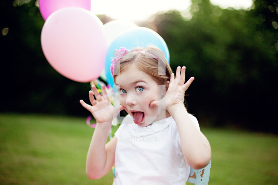 girl child holding balloons making silly faces