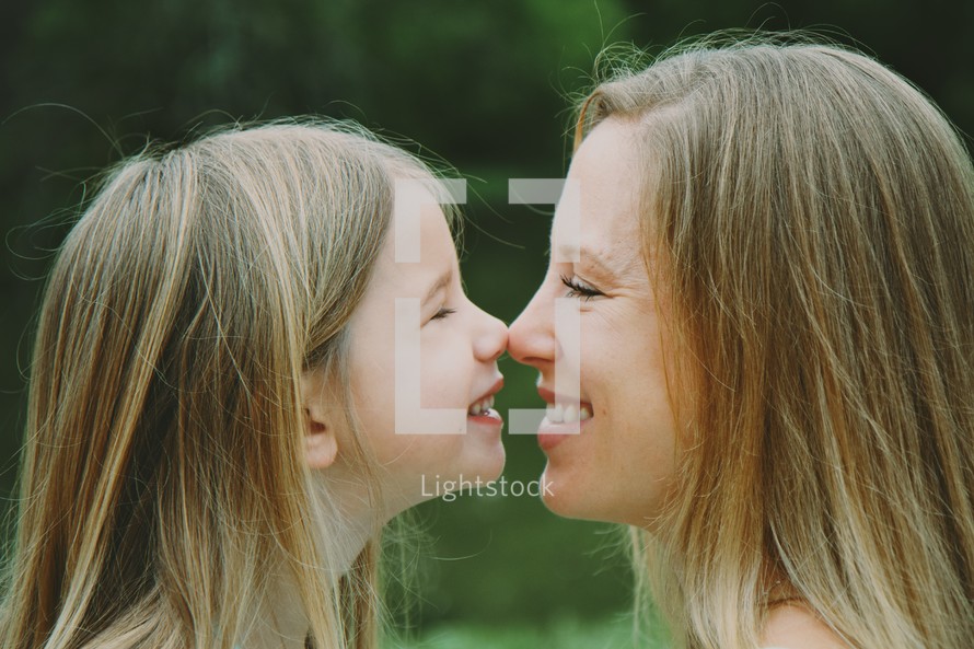Mother and daughter touching noses outside.