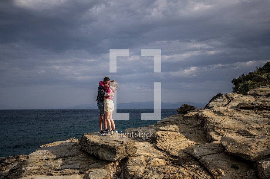 a couple hugging on a rocky shore 