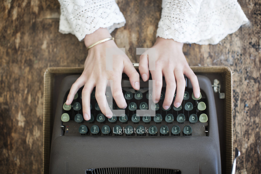 Hands typing on a vintage typewriter.
