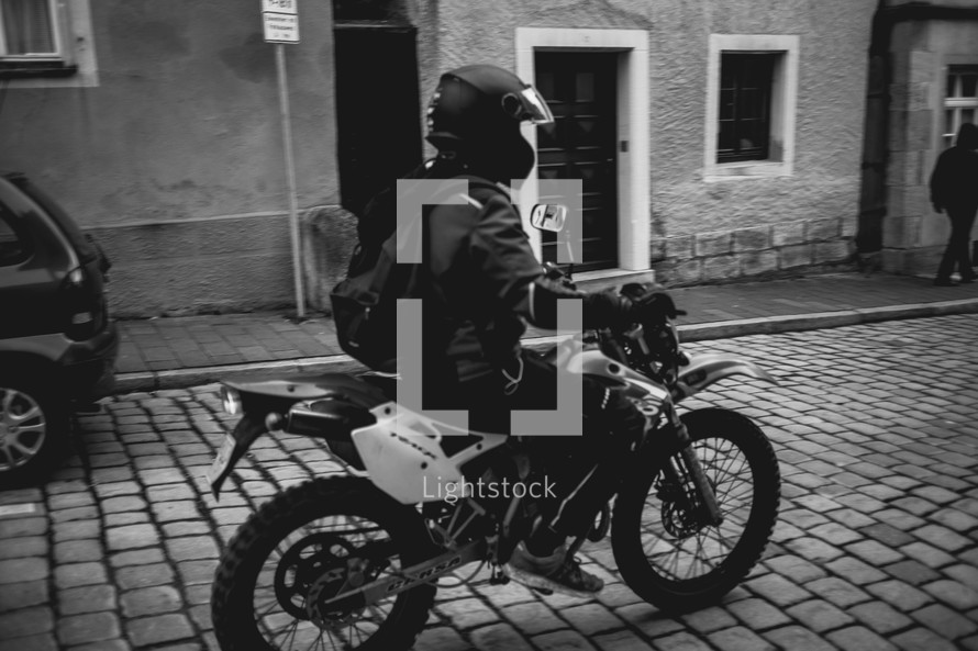 man riding a motorbike on a cobble stone street 