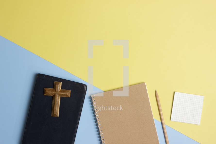 cross, BIble, and notebook on a pink and yellow background 