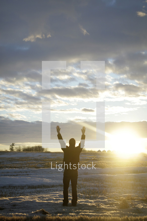 man standing with raised arms in a snow covered field 