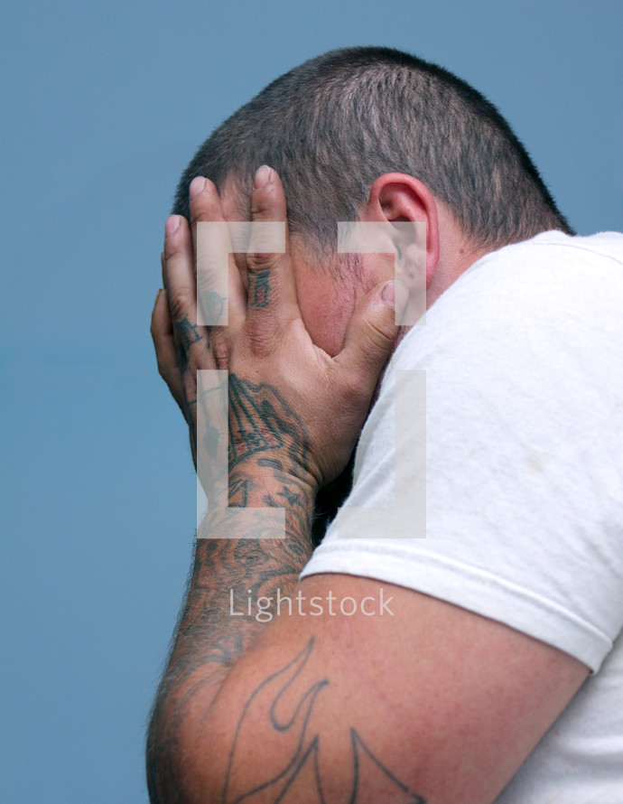 man with tattooed hands covering his face