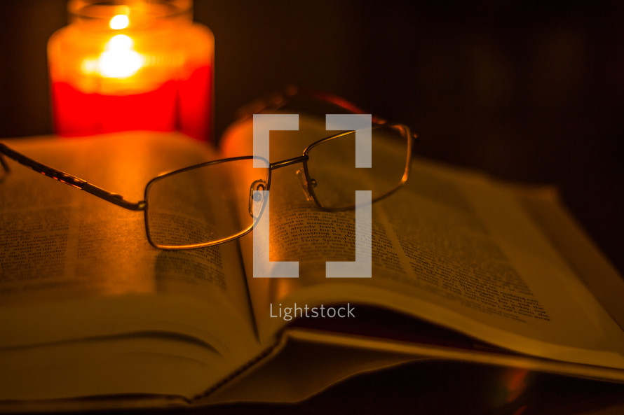 reading glasses on the pages of a Bible and a candle 