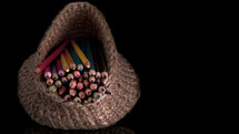 Many colored pencils in a knitted basket on a black background