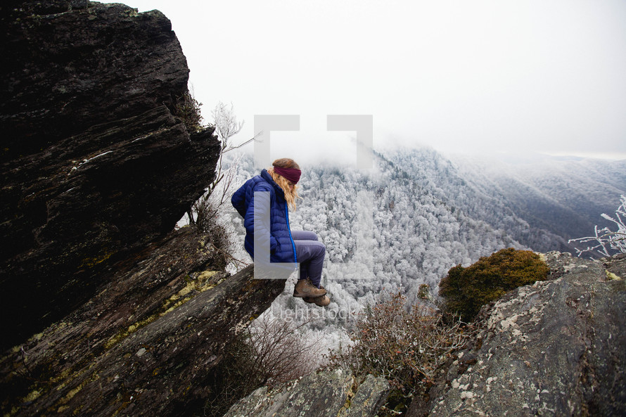 a woman sitting on a rock on a winter mountain 