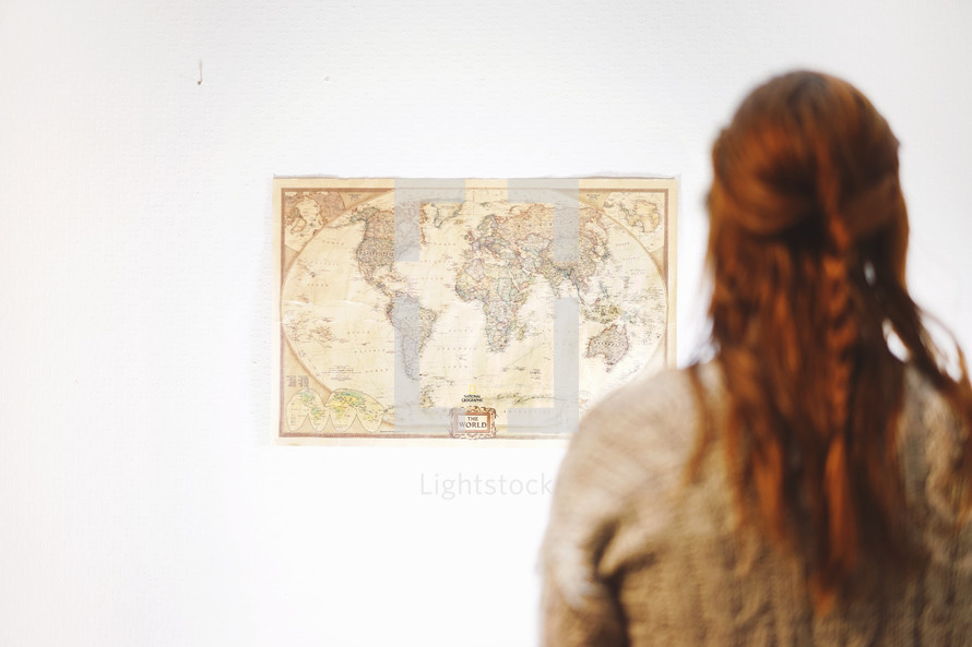 a woman looking at a world map on a wall 