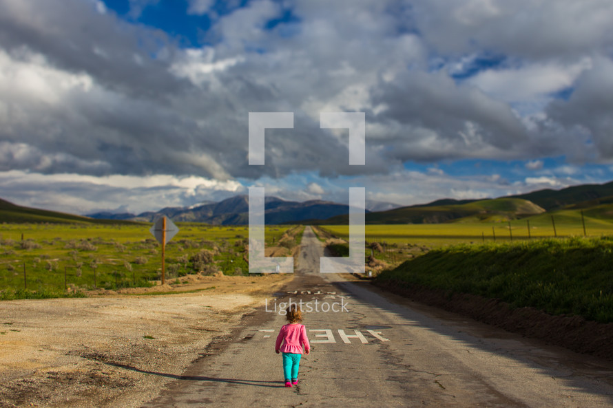 toddler girl walking down a rural road 