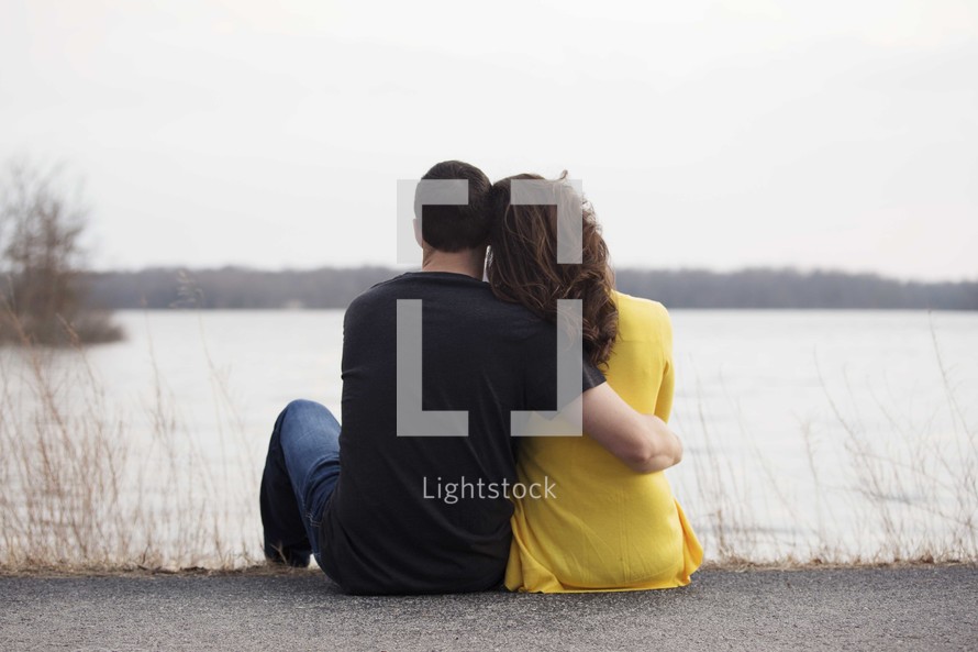 a couple sitting by a lake with backs to the camera 