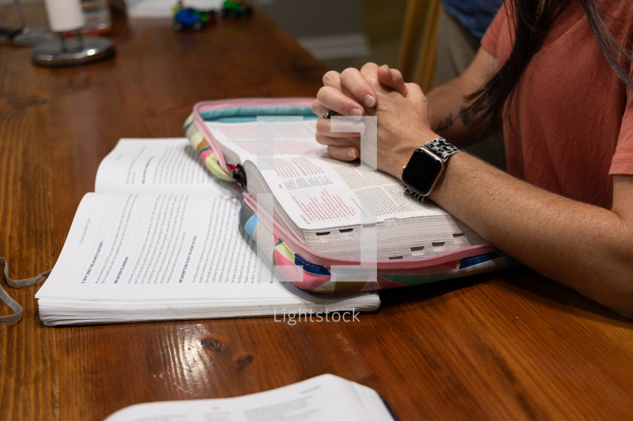 Woman's folded hands in prayer resting on open Bible during Bible study time in discipleship group